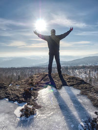 Standing man with raised arm on icy stone and looking on snow covered mountains. winter landscape 