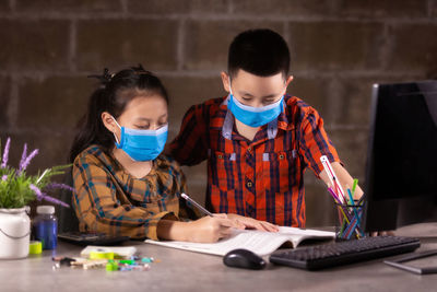 View of boy and girl wearing flu mask studying at home