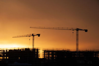 Silhouette cranes at construction site against sky during sunset