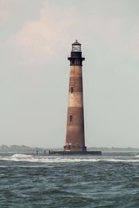 Lighthouse by sea against sky