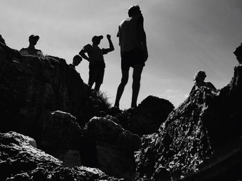 Low angle view of people standing on rock against sky