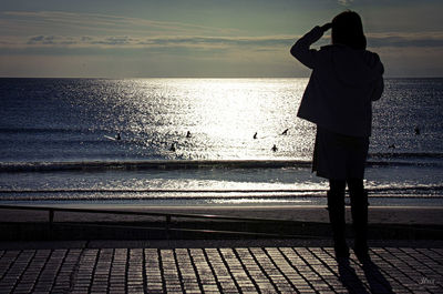 Rear view of man photographing sea against sky during sunset
