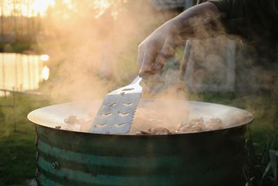 Cropped hand of person making food in container at backyard during sunset