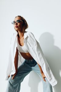 Young woman wearing sunglasses while standing against white wall