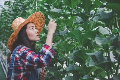 Woman standing by plants at greenhouse