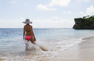 Woman wearing bikini standing on shore at beach