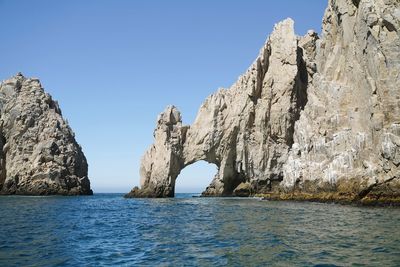 Rock formations in sea against clear blue sky