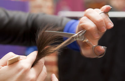 Cropped hands of hairdresser cutting customer hair at salon