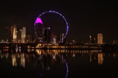 Illuminated buildings by river against sky at night