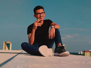Young man looking away while sitting against sky