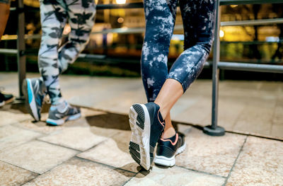 Woman runner with crossed legs resting next to female friends after training at night on town