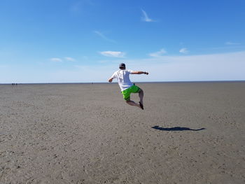 Rear view of man jumping at beach against sky during sunny day