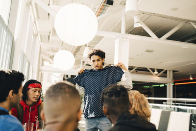 Teenage boy showing new t-shirt to friends while standing in restaurant at shopping mall