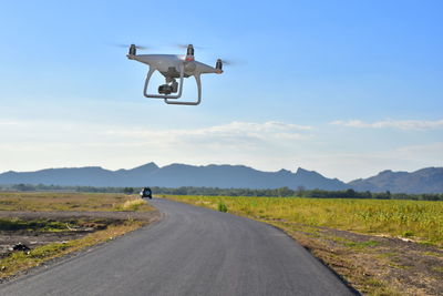 Drone flying over road against sky