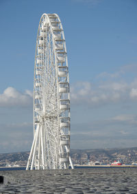 Ferris wheel by sea against sky