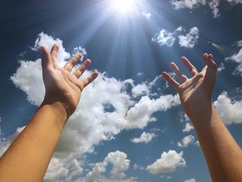 Low angle view of person hands praying against sky