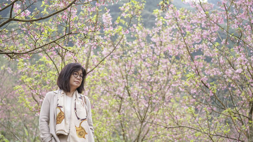 Young woman standing by cherry blossom tree