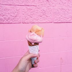 Close-up of hand holding ice cream cone by wall