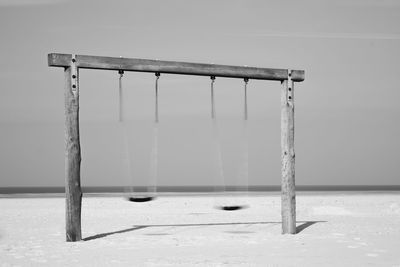 Empty swing on beach against sky