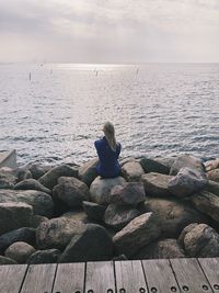 Rear view of woman sitting on rock against sea at beach