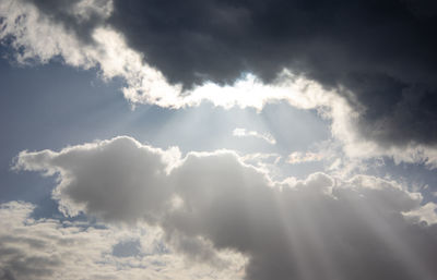 Low angle view of sunlight streaming through clouds