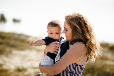 Grandmother holding & snuggling grandson while standing on beach