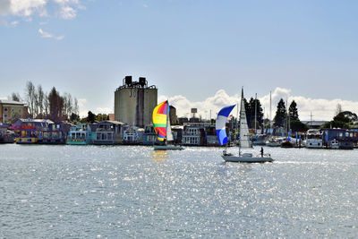 Sailboats in sea by buildings against sky