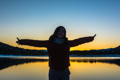 Happy teenage girls standing by lake against clear sky during sunset