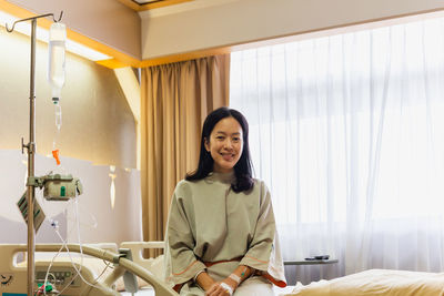 Front view of asian woman patient sitting on hospital bedroom smiling at camera with dropper