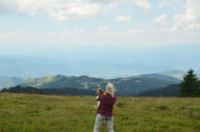 Rear view of woman photographing on mountain against sky