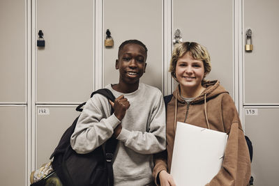 Portrait of smiling male and female teenage friends standing against locker in school