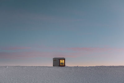 Built structure on snow covered land against sky during sunset