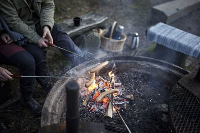 People preparing hotdogs over campfire