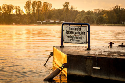 Information sign by river against sky during sunset