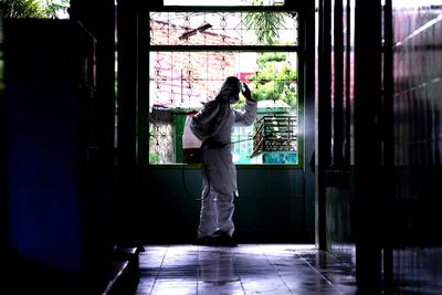 Healthcare worker in uniform standing by window during lockdown