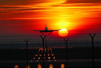 Airplane flying over runway against sky during sunset