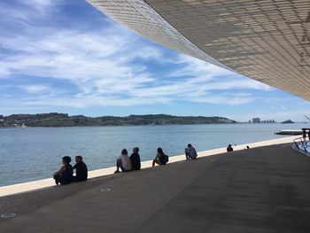 People sitting by sea against sky