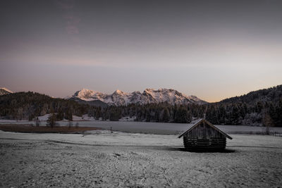Built structure on snow covered land against sky during sunset