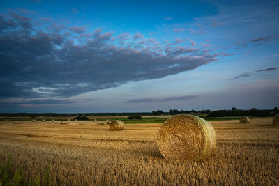 Hay bales on stubble, clouds after sunset in the sky