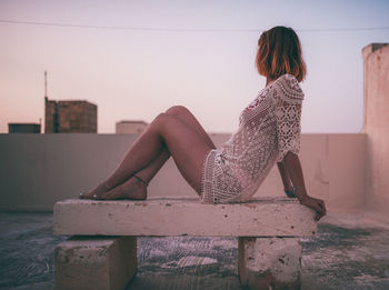 Side view of woman sitting on seat against sky