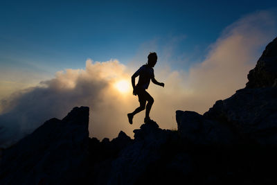 Silhouette of man on rocky ridge in mountain running uphill