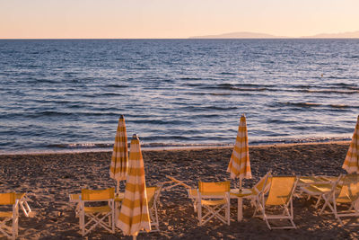 Chairs on beach against sky during sunset