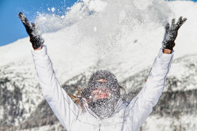 Cheerful woman throwing snow while standing against mountains