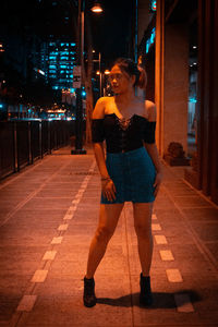 Full length portrait of young woman standing in illuminated city