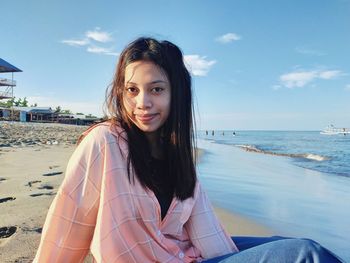 Portrait of beautiful young woman on beach against sky