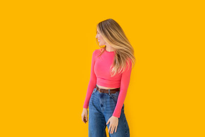 Young woman standing against yellow background