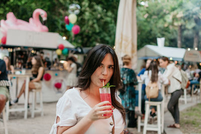 Beautiful young woman drinking strawberry mojito cocktail in park in city