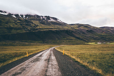 Dirt road leading towards mountains against sky