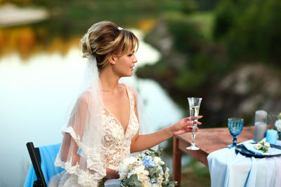Bride at the wedding table with a glass of sparkling wine in the background of the river