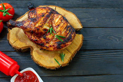 Baked part of tasty chicken, with golden brown crust, cooked on grill or barbecue on wooden table. 